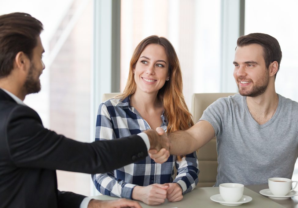 Happy couple handshaking a consulting agent in an office